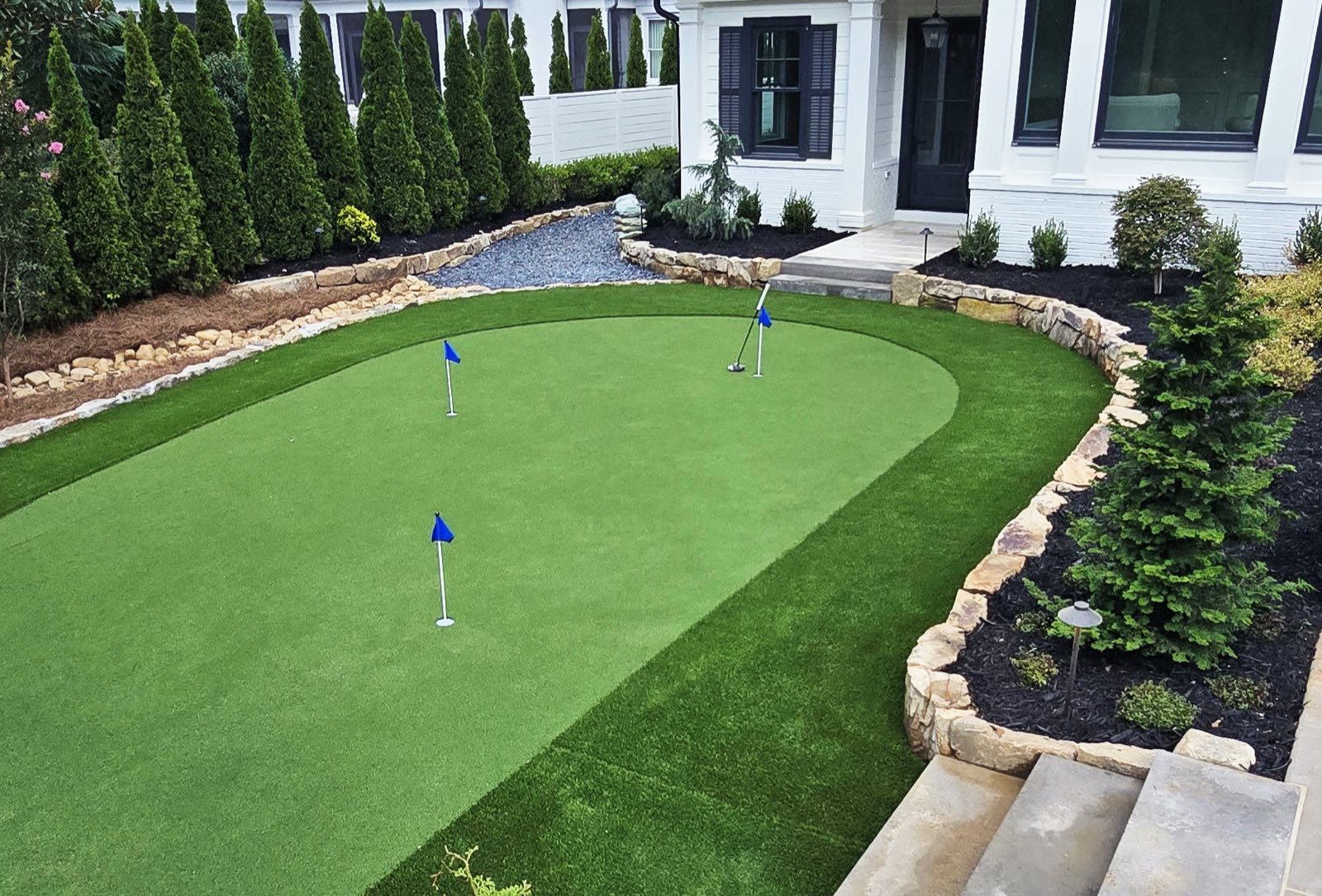 Front-yard putting green with blue flags, edged in stone-lined planting beds