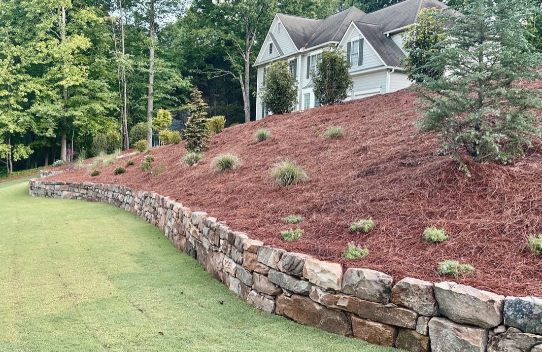 Stacked stone retaining wall holding a planted slope